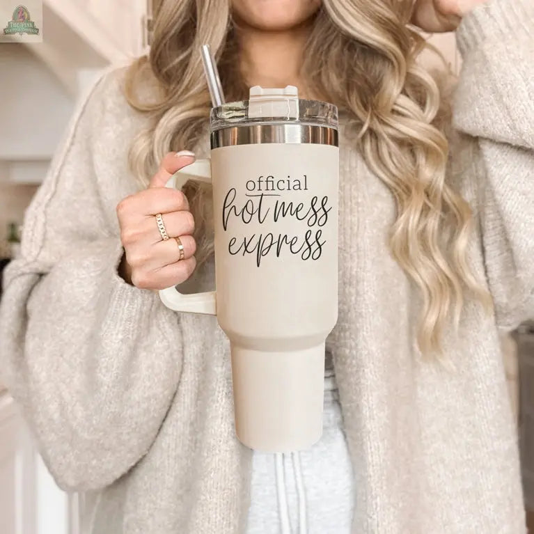 A woman with long, wavy blonde hair in a cozy beige sweater holds the Official Hot Mess 40oz tumbler with a straw.