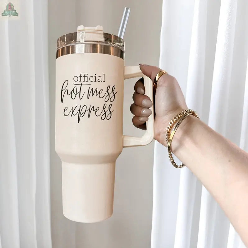A manicured hand with gold bracelets holds the Official Hot Mess 40oz tumbler with lid and straw, featuring bold script. White curtains create an elegant backdrop.