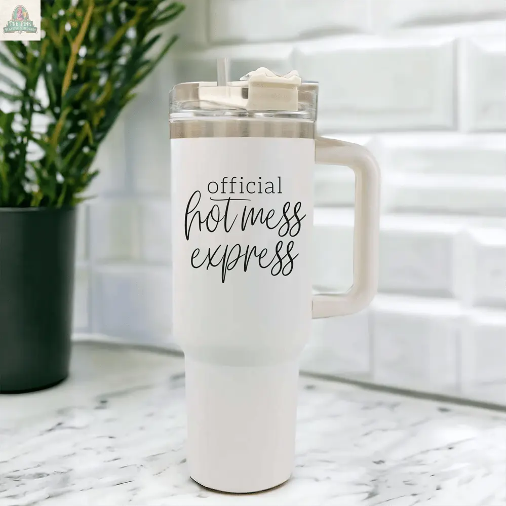 The Official Hot Mess 40oz white insulated mug with handle and clear lid sits on a marble countertop, featuring "Official Hot Mess Express" in black script. A green potted plant is in the background—ideal for your daily caffeine fix.