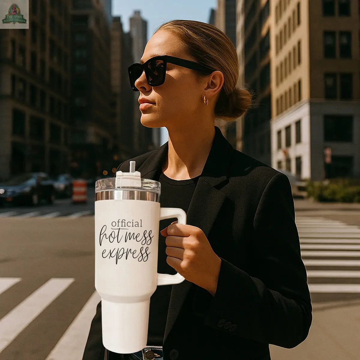 A woman in sunglasses and a black blazer stands on a city street holding the Official Hot Mess 40oz insulated tumbler with a straw.