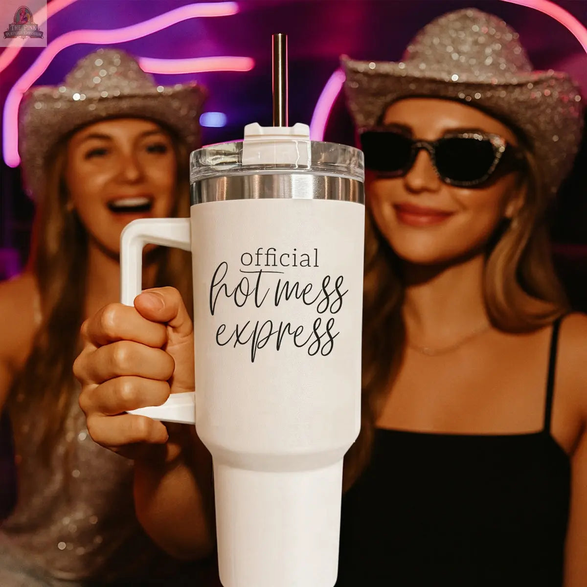 Two women in sparkly hats and sunglasses smile at a party as one holds the 40oz insulated Official Hot Mess tumbler. Neon lights glow behind them, perfectly matching their festive vibe.