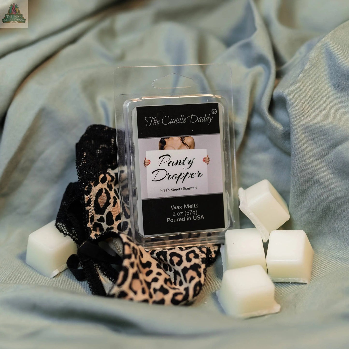 A 2oz pack of PANTY DROPPER Fresh Bed Sheets scented wax melts rests on light blue fabric beside white aromatherapy wax melts and black and leopard lace panties.