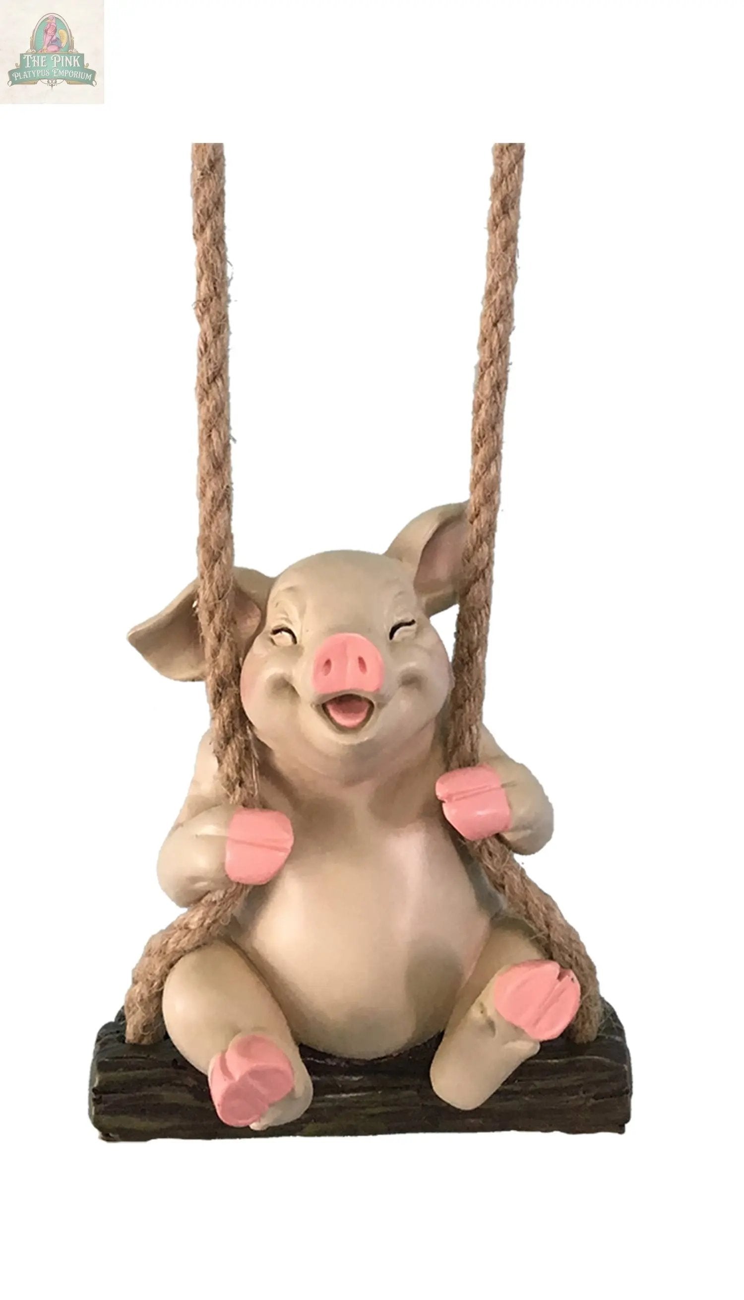 The PIG SWINGER is a handcrafted figurine with pink ears, snout, and hooves, sitting cheerfully on a wooden swing with thick rope. Ideal for outdoor décor, this playful piece adds charm and stands out against any plain white background.