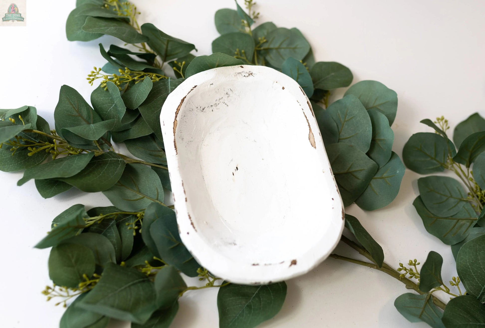 A handmade Petite Wood Bowl (9-10", Natural, 10x6x3) from Mexico with a rustic finish is displayed atop green leafy branches on a white background.