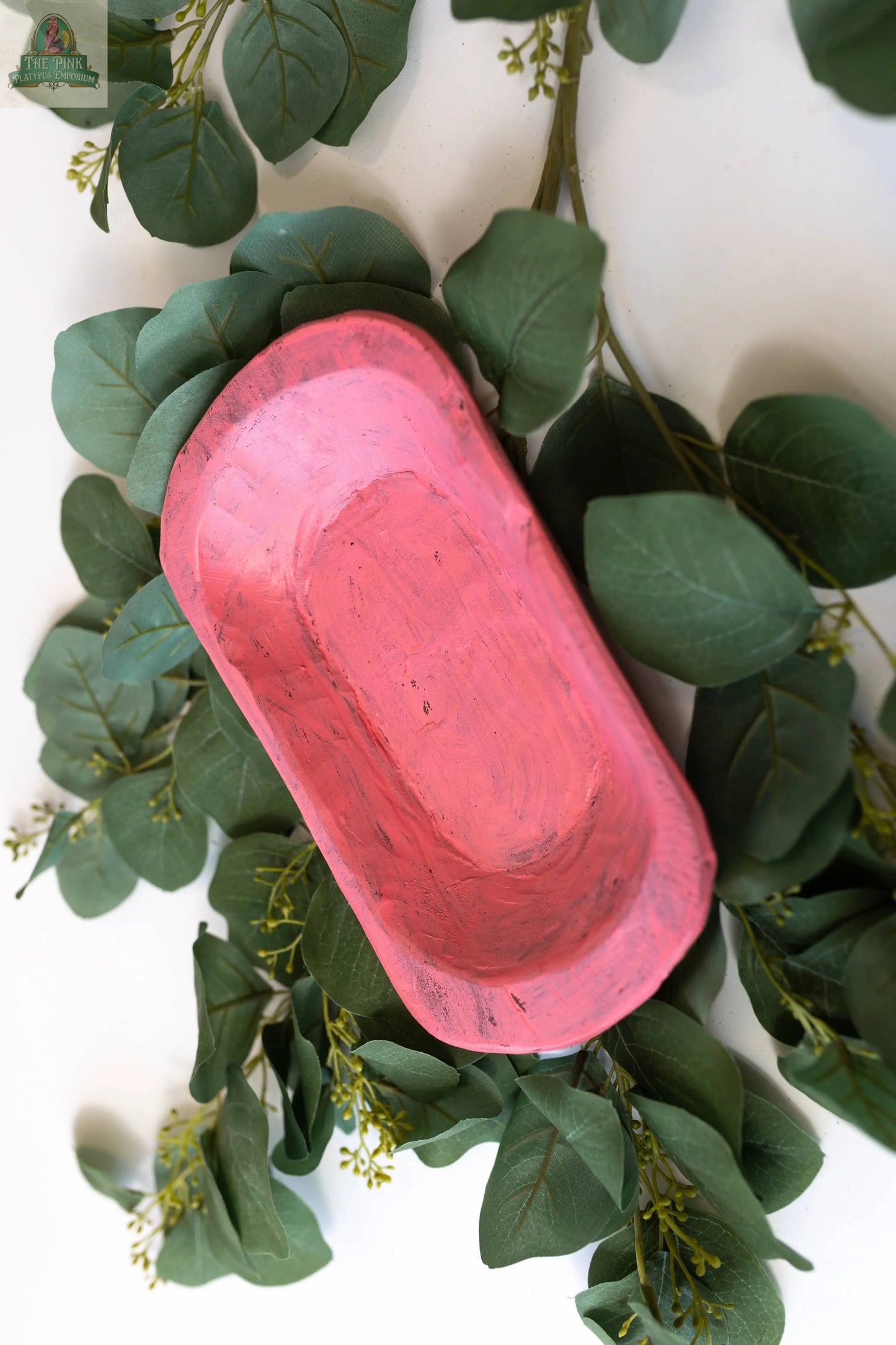A Handmade in Mexico Petite Wood Bowl (9-10", Natural, 10x6x3) rests on a surface with green leafy branches, highlighting the contrast between the natural wood bowl and the surrounding greenery.
