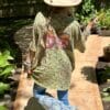 Person wearing a cowboy hat and graphic tshirt  standing on a stone path with greenery around