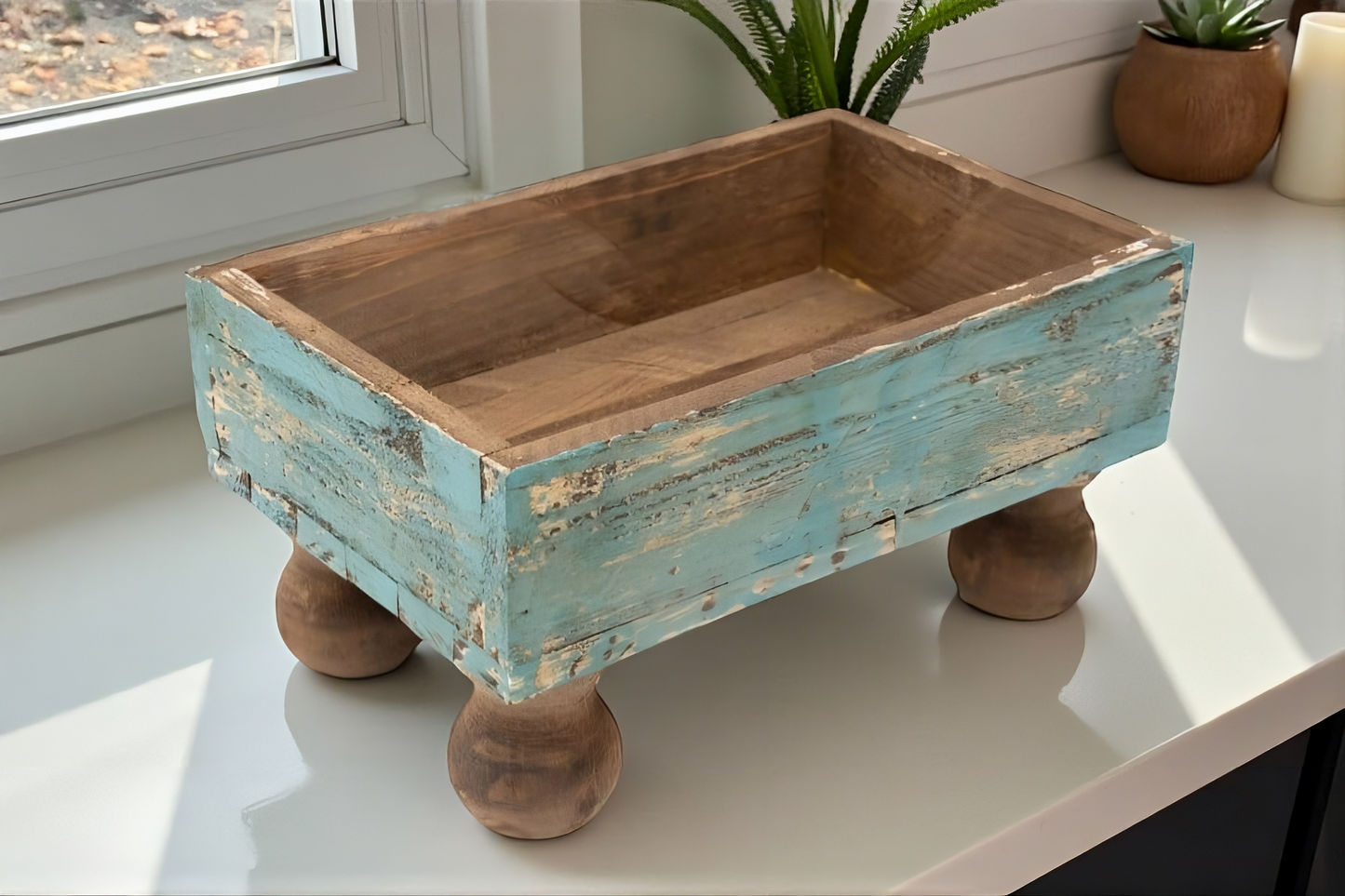 Wooden planter box with distressed turquoise paint on a white surface near a window.