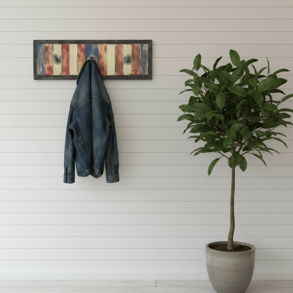 Denim jacket hanging on an americana wooden wall art coat hook next to a potted plant against a white paneled wall.