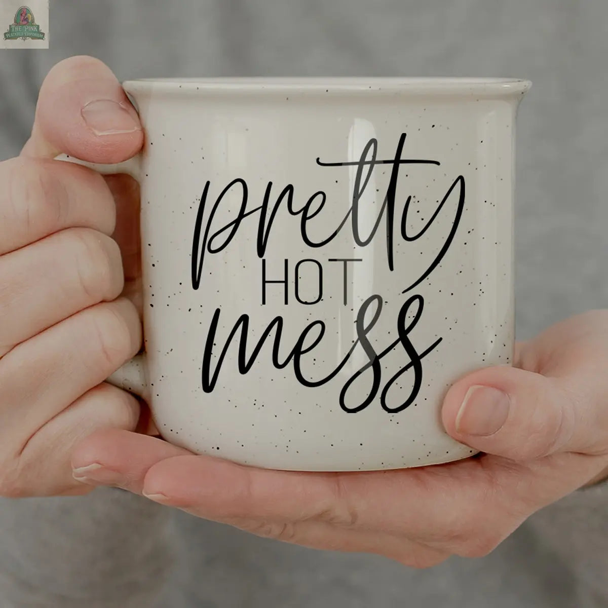 A person holds the Pretty Hot Mess 14.5oz white ceramic mug with black script, focusing on their hands and the microwave safe mug against a blurred background.