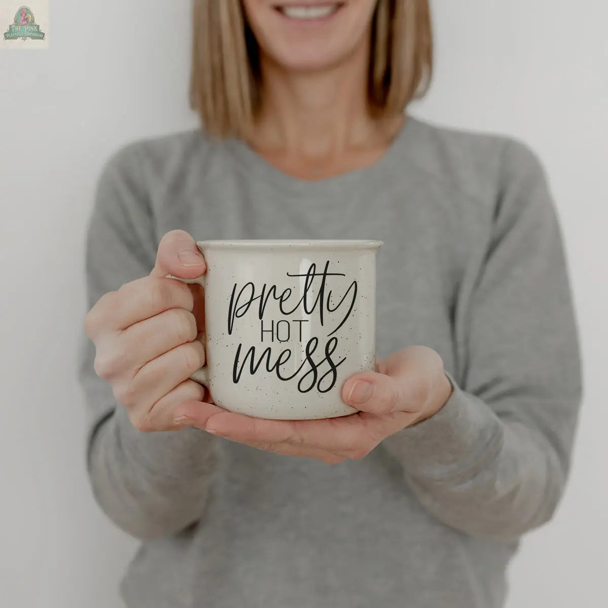 A woman in a gray sweater holds the 14.5oz Pretty Hot Mess ceramic mug, featuring black text. Her face is partially out of frame, and the plain light background keeps the focus on the dishwasher safe mug.