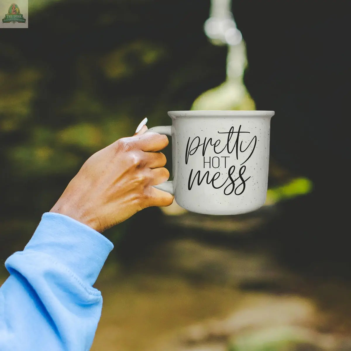 A person in a light blue sweatshirt holds the Pretty Hot Mess 14.5oz white ceramic mug, featuring "pretty hot mess" in stylish script. The mug is microwave safe, and the blurred outdoor background adds a relaxed vibe.