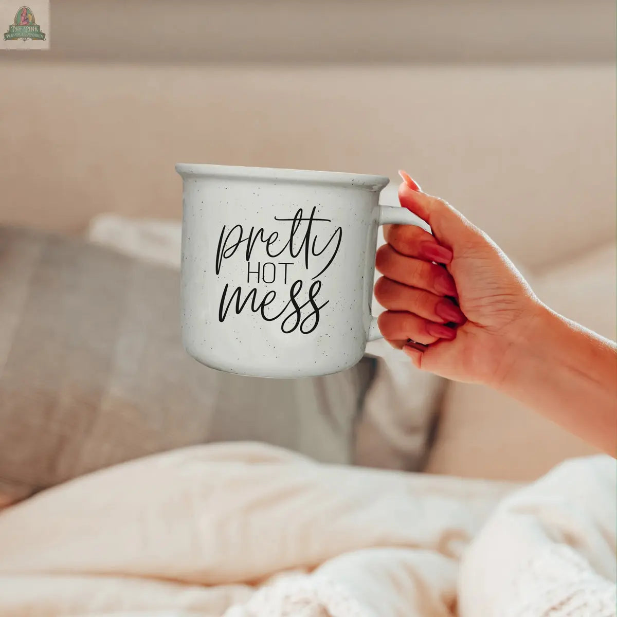 A hand holds the Pretty Hot Mess 14.5oz ceramic mug in a cozy bedroom with pillows and bedding—perfect for sipping your favorite microwave-safe drinks.