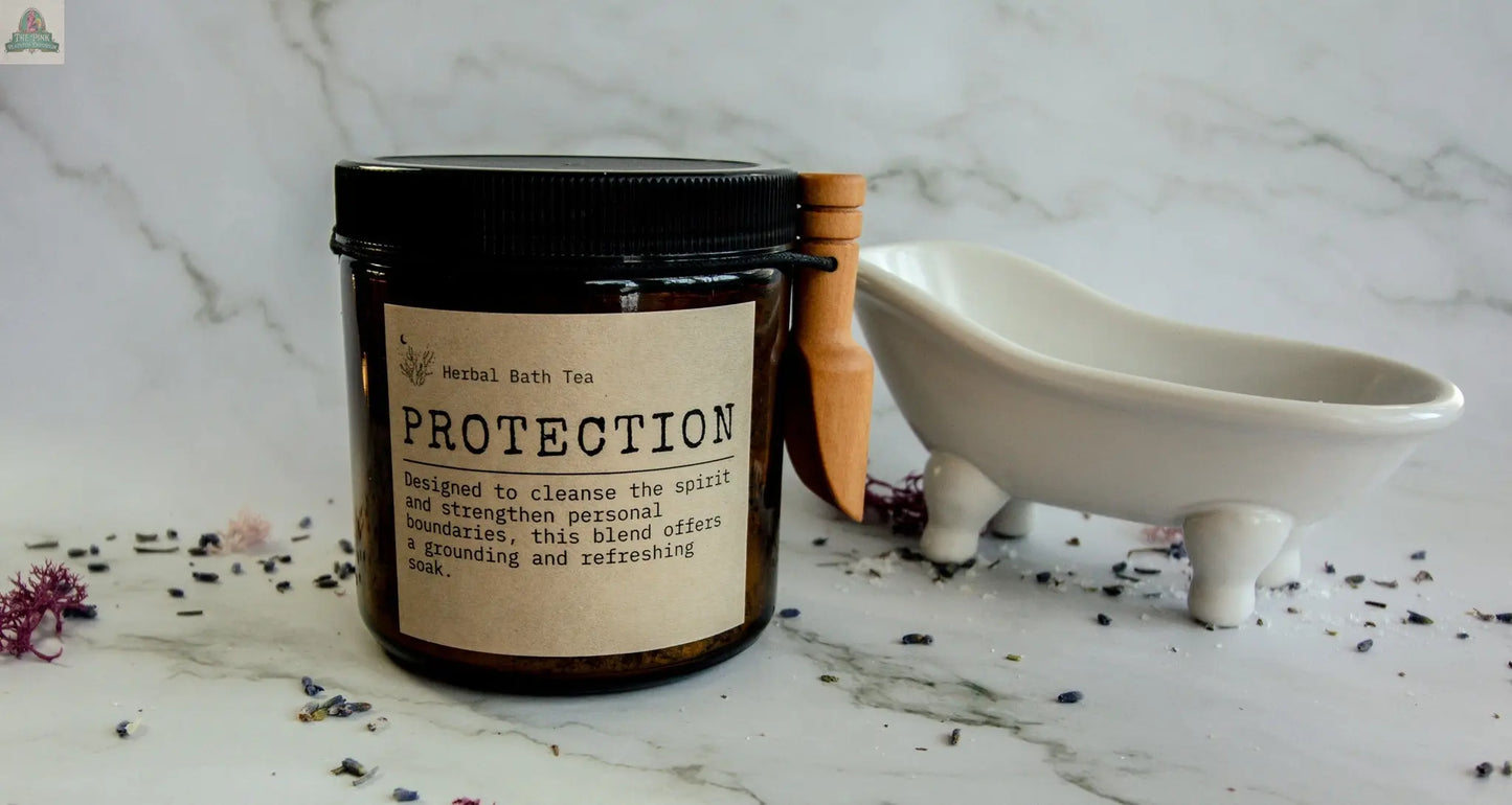 A jar labeled "Protection" rests on a marble surface with dried flowers, a wooden scoop, and a tiny white bathtub beside it—the ideal set for your next protective bath soak.