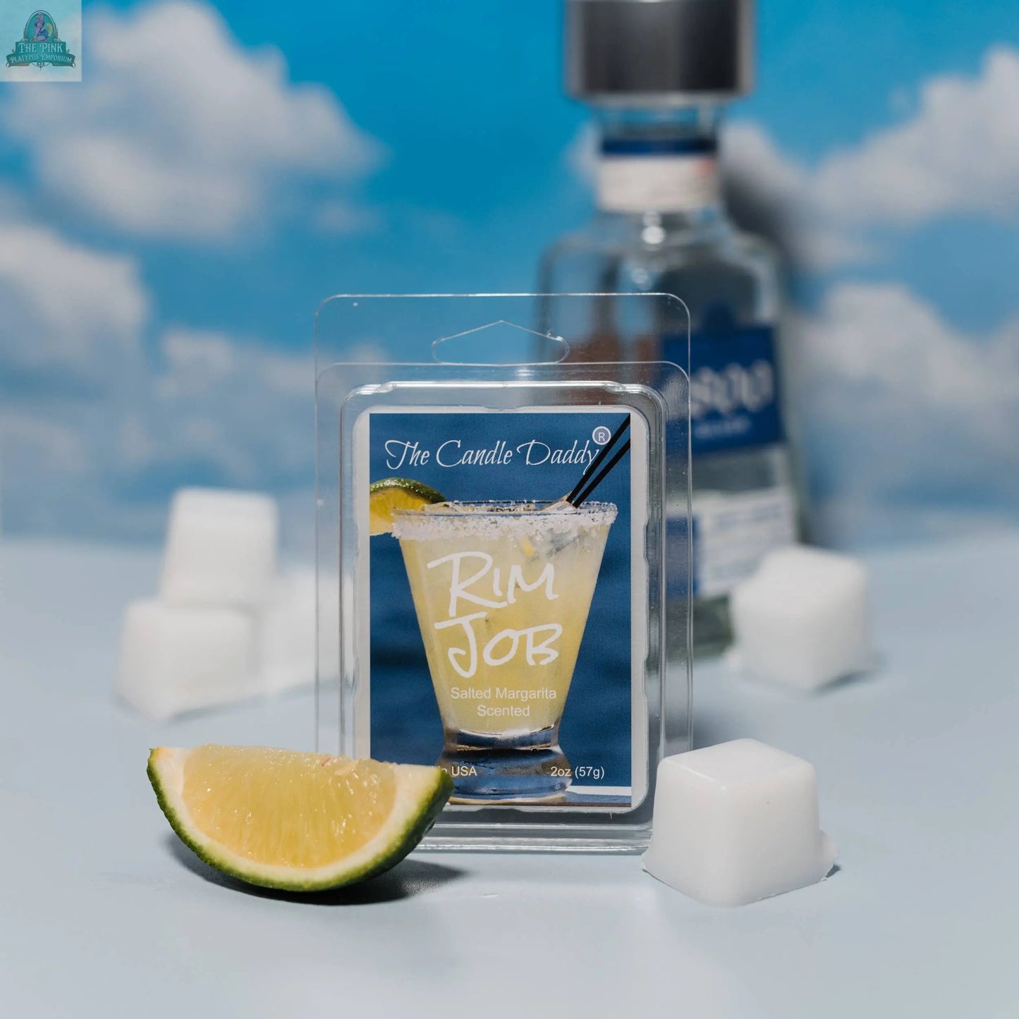 A 2 oz pack of RIM JOB Salted Margarita Scented Wax Melt sits upfront with a lime wedge and white cubes beside it, while a tequila bottle and blue sky with clouds add to the lively background.