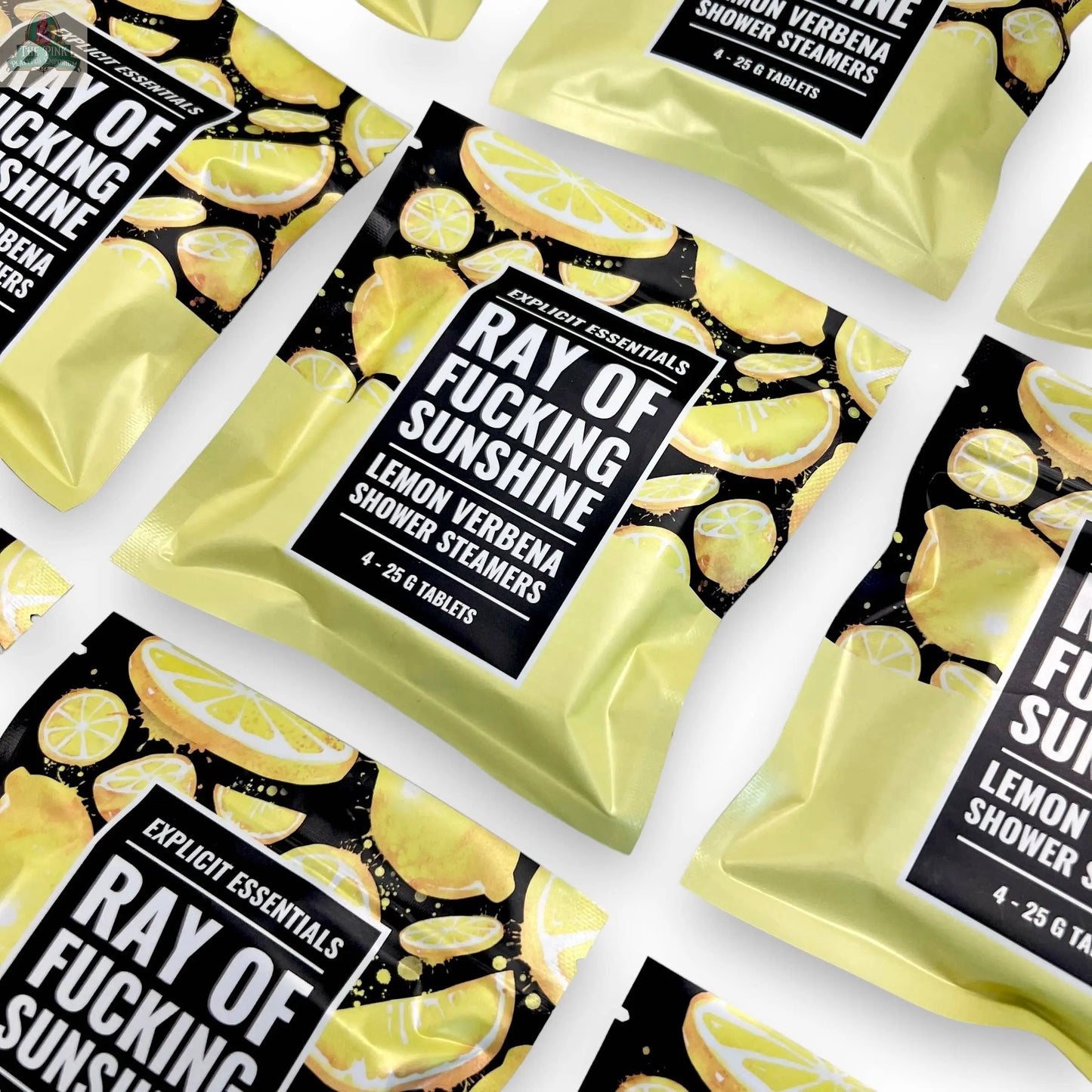 Several Ray of F&cking Sunshine Shower Steamers by Explicit Essentials are arranged diagonally on a white background. The yellow packets, decorated with lemon slices, highlight the refreshing essential oils inside.