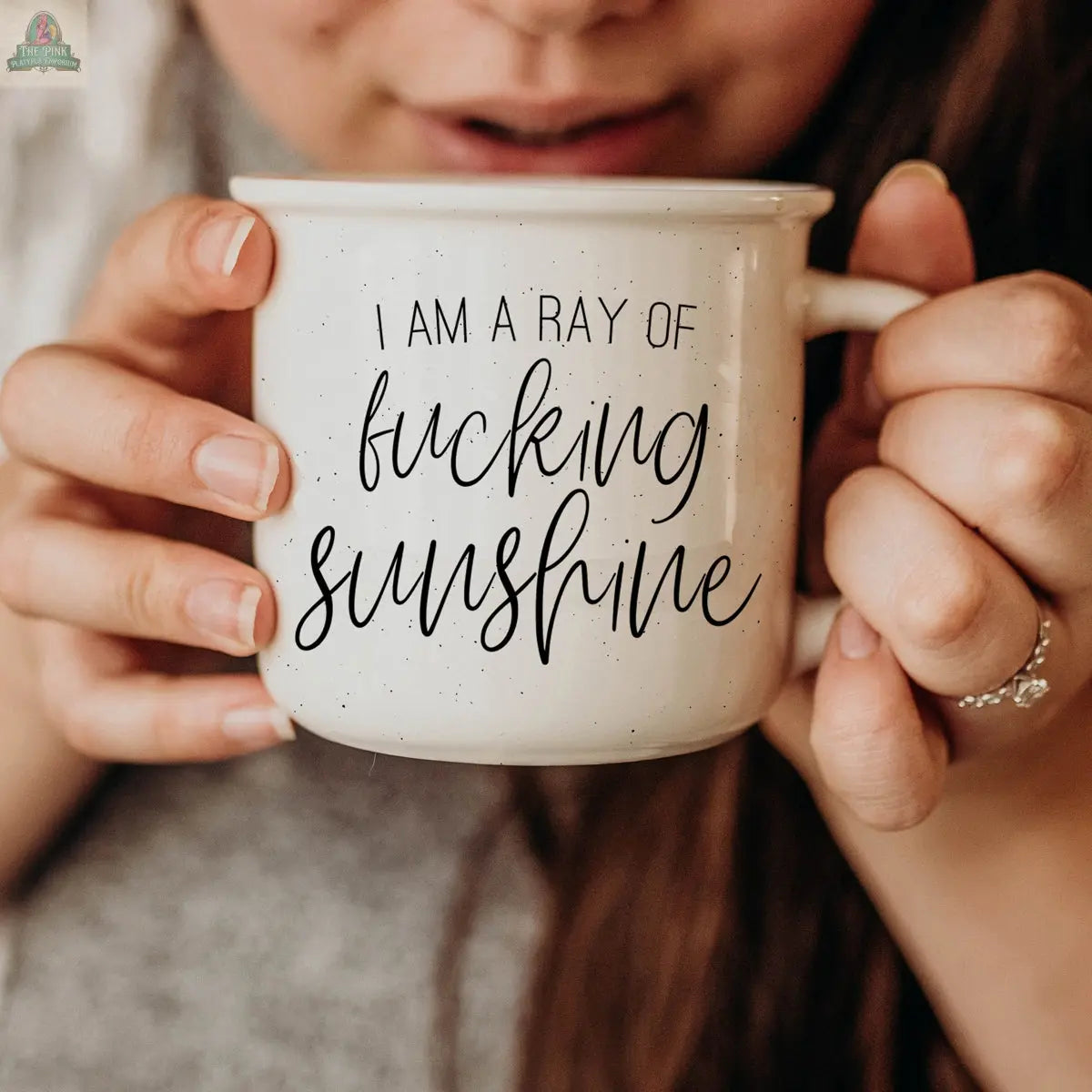 A person holds the Ray of F'n Sunshine 14.5oz ceramic mug, featuring bold black text and a sunny design—perfect for anyone with a sarcastic side. Their face is partially visible, and they're wearing a gray top.