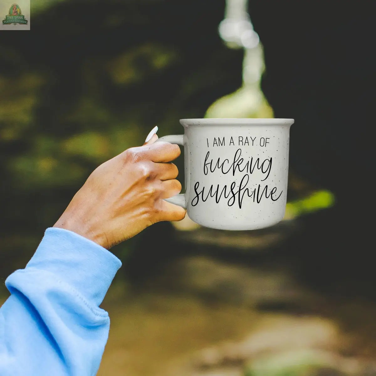 A person in a light blue sleeve holds the Ray of F'n Sunshine 14.5oz white ceramic mug, featuring its bold message, against a blurred outdoor background.