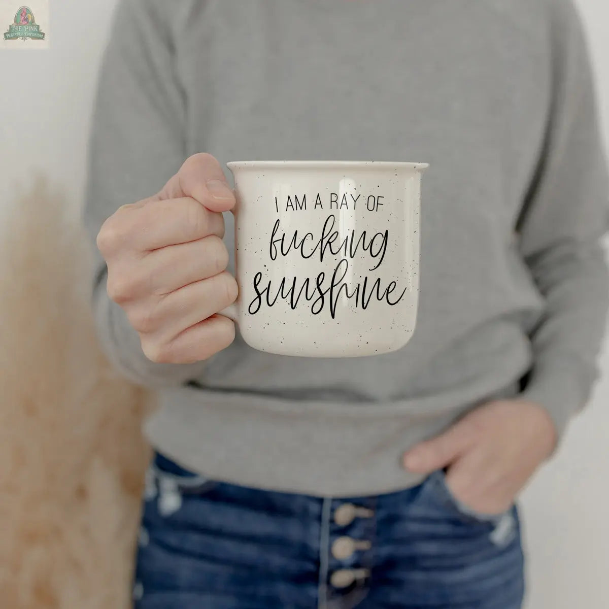 A person in a grey sweater and blue jeans holds the "Ray of F'n Sunshine 14.5oz" coffee mug.