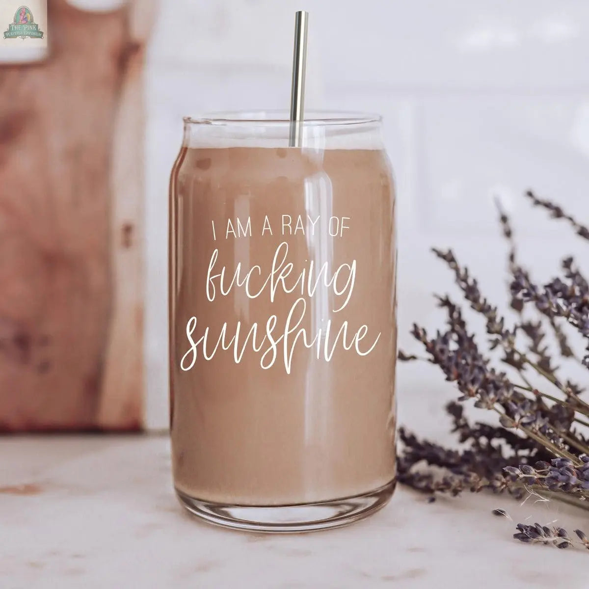 The Ray of Sunshine 17oz is a glass drinking cup with a bamboo lid, filled with a brown liquid, and comes with a stainless steel straw.