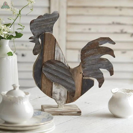 The Reclaimed Wood Rooster sits on a wooden table, surrounded by white ceramic dishes and a flower vase, adding farmhouse charm to a white shiplap setting.