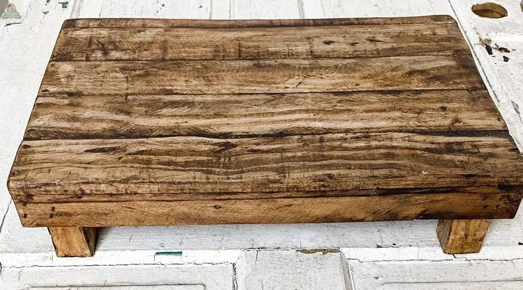 The Rectangular Wood Stool, Natural, Handmade, features visible grain patterns and signs of use. With four short legs and a rustic look, it adds charm to your home decor when displayed on any surface.
