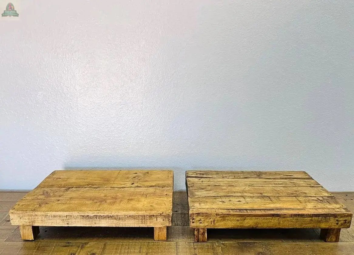 Two handmade, natural rectangular wood stools with short legs are placed side by side on a wooden floor against a plain light wall, adding charm to any rustic home decor.