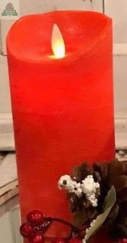 A Red LED Pillar Candle w/Timer sits on a surface, surrounded by a pine cone, artificial white berries, and red berries, while the softly blurred background adds a warm, inviting ambiance.