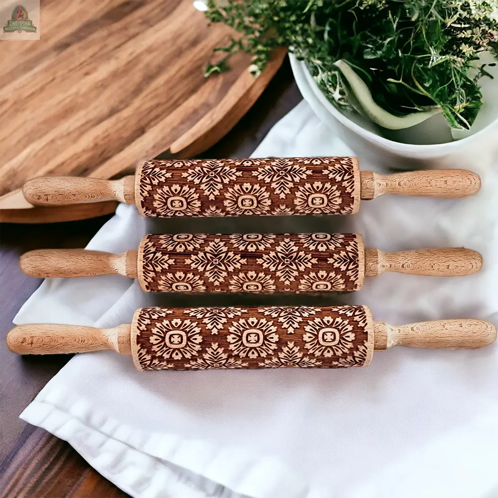 Three Box Style wooden rolling pins with intricate floral carvings rest on a white cloth—perfect for baking gifts. A wooden tray and a white bowl with greenery sit in the background on a wooden surface.