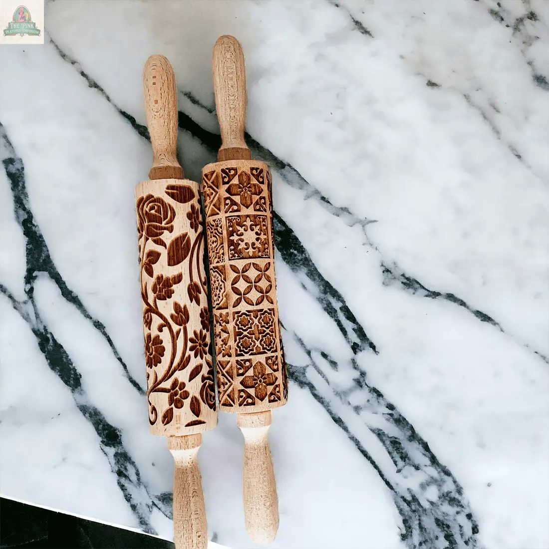 Two Rolling Pins - Box Style, one with a floral and one with a geometric engraved pattern, rest on a white marble surface with dark veins. Perfect baking gifts, they pair beautifully with your favorite cookie cutters.