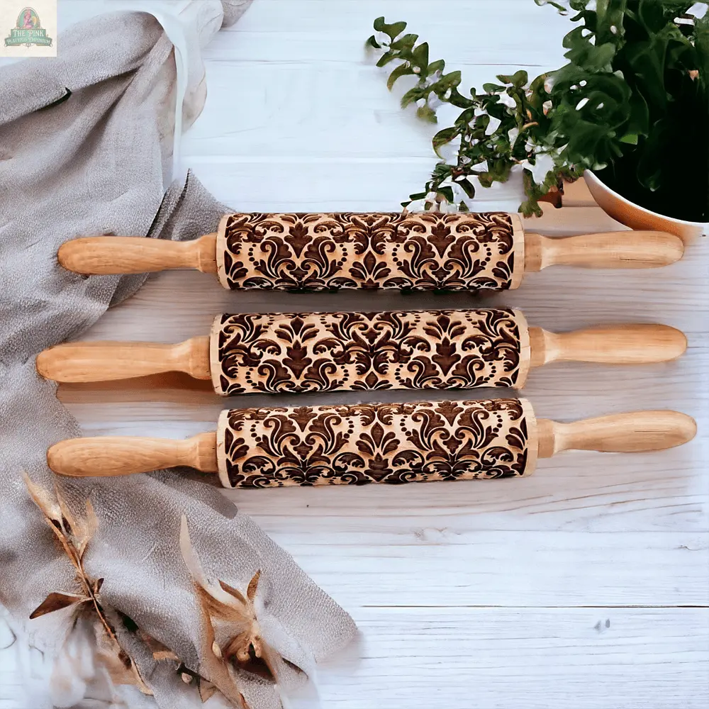 Three Rolling Pins - Box Style, featuring ornate engraved patterns, are arranged parallel on a white wooden surface with decor—ideal baking gifts for any kitchen lover.