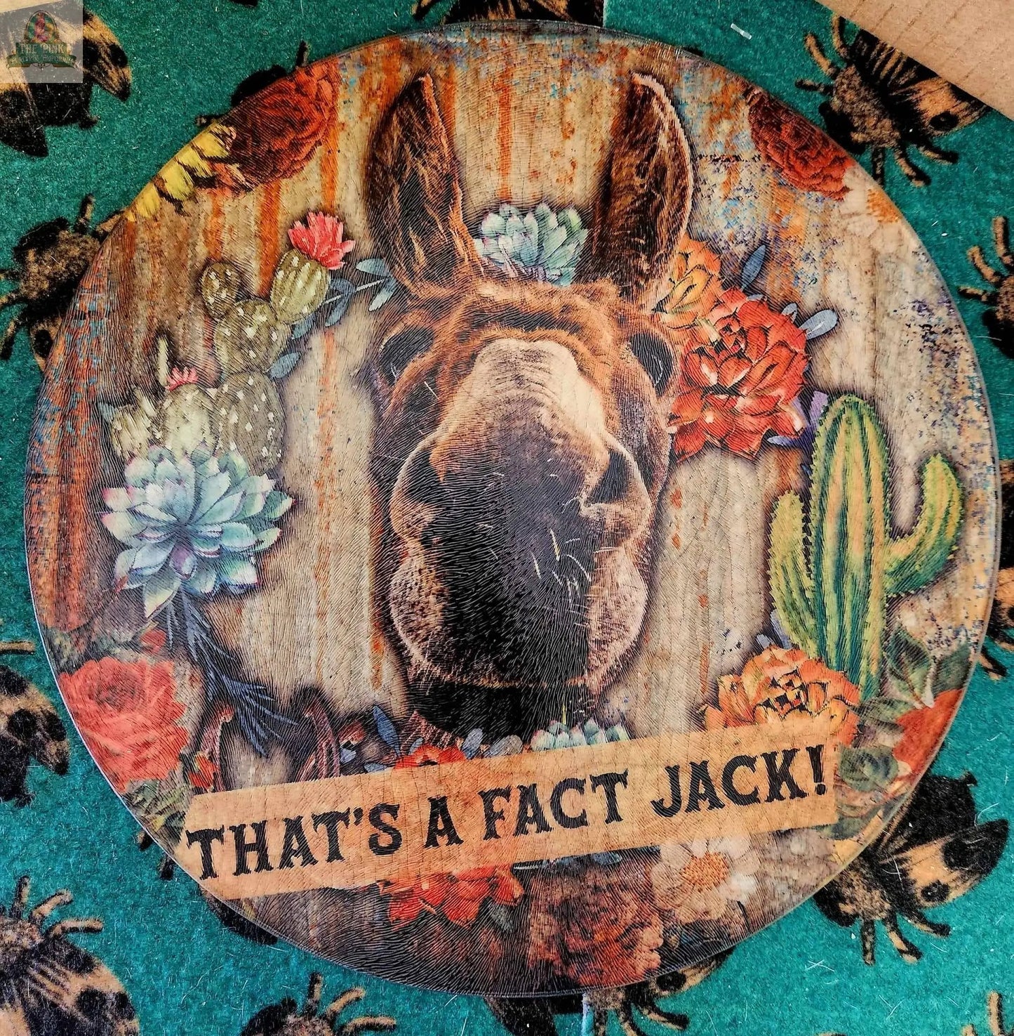 The Large 12" Round Glass Cutting Board/Charcuterie/Trivet features a donkey’s face with vibrant cacti and flowers, a “THAT'S A FACT JACK!” banner, and a rustic wood background—perfect for serving or kitchen décor.