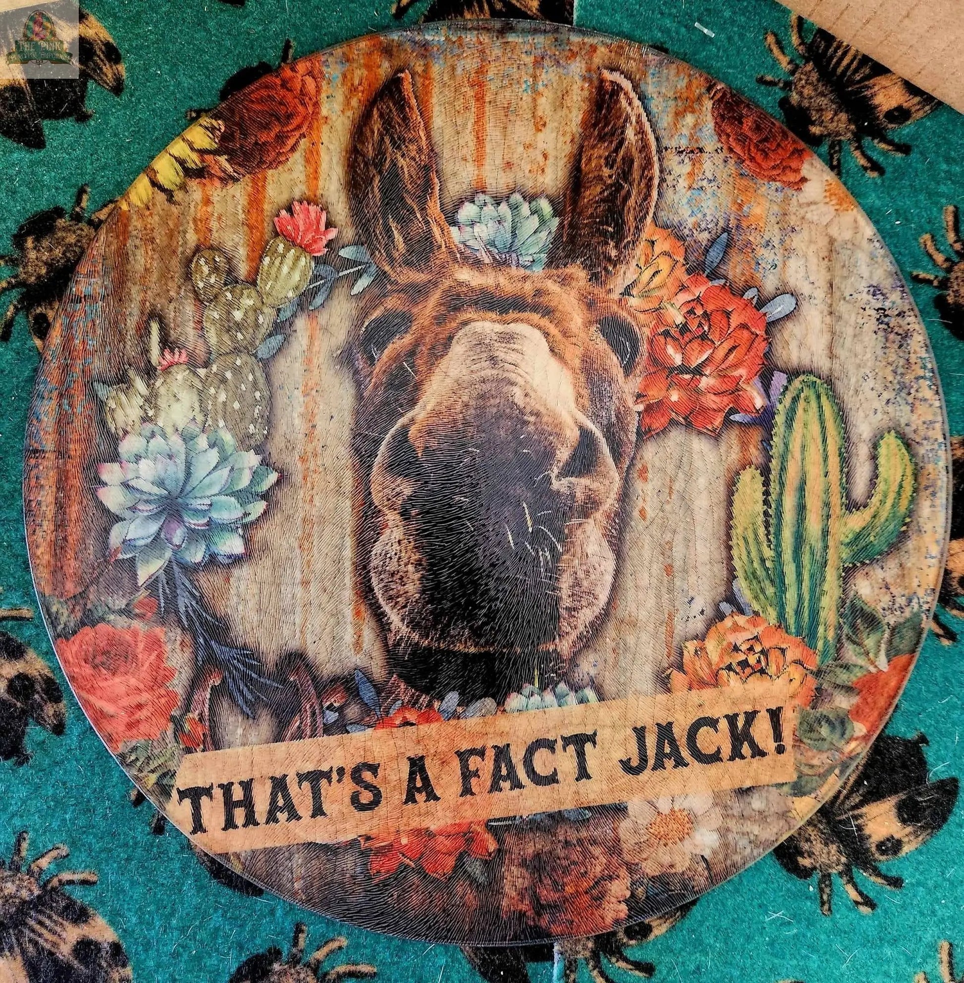 The Large 12" Round Glass Cutting Board/Charcuterie/Trivet features a donkey’s face with vibrant cacti and flowers, a “THAT'S A FACT JACK!” banner, and a rustic wood background—perfect for serving or kitchen décor.