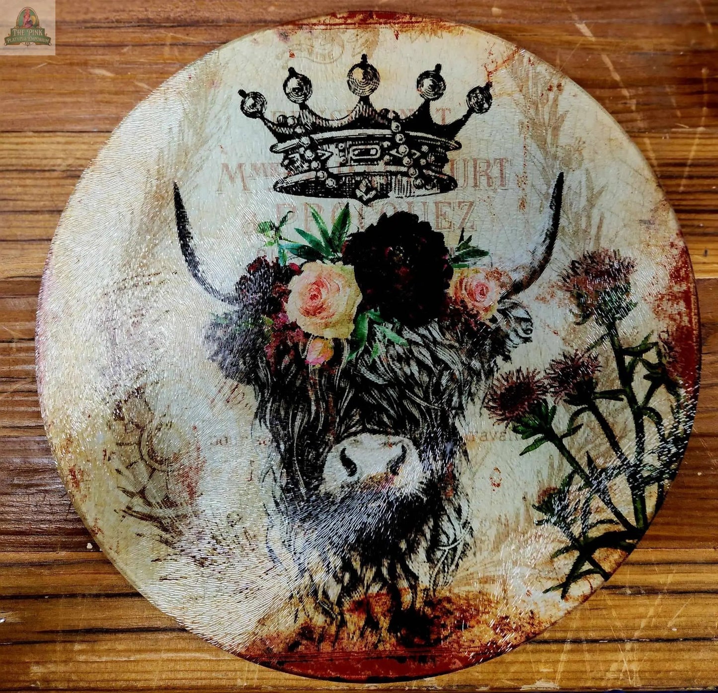 An 8" round glass cutting board, charcuterie, or trivet featuring a crowned highland cow with flowers on a vintage floral background—ideal rustic kitchen décor.