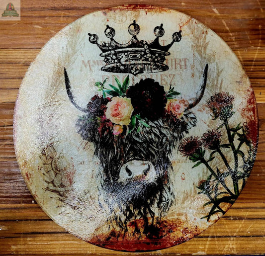 An 8" round glass cutting board, charcuterie, or trivet featuring a crowned highland cow with flowers on a vintage floral background—ideal rustic kitchen décor.