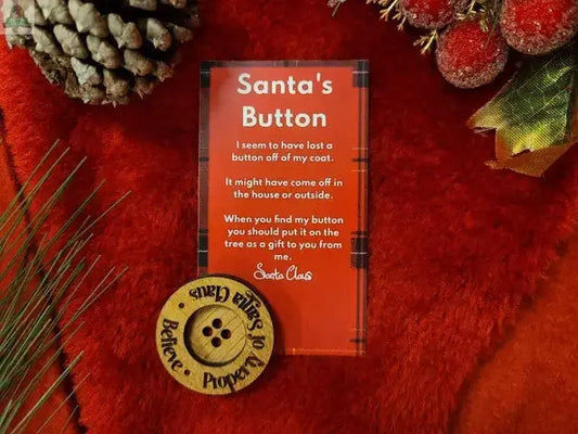 A festive red scene features pine cones, Christmas decor, and Santa's Button—a large keepsake etched "Santa Claus 30, Believe, Property Of," with a card explaining how Santa lost his coat button. A charming ornament rests nearby.