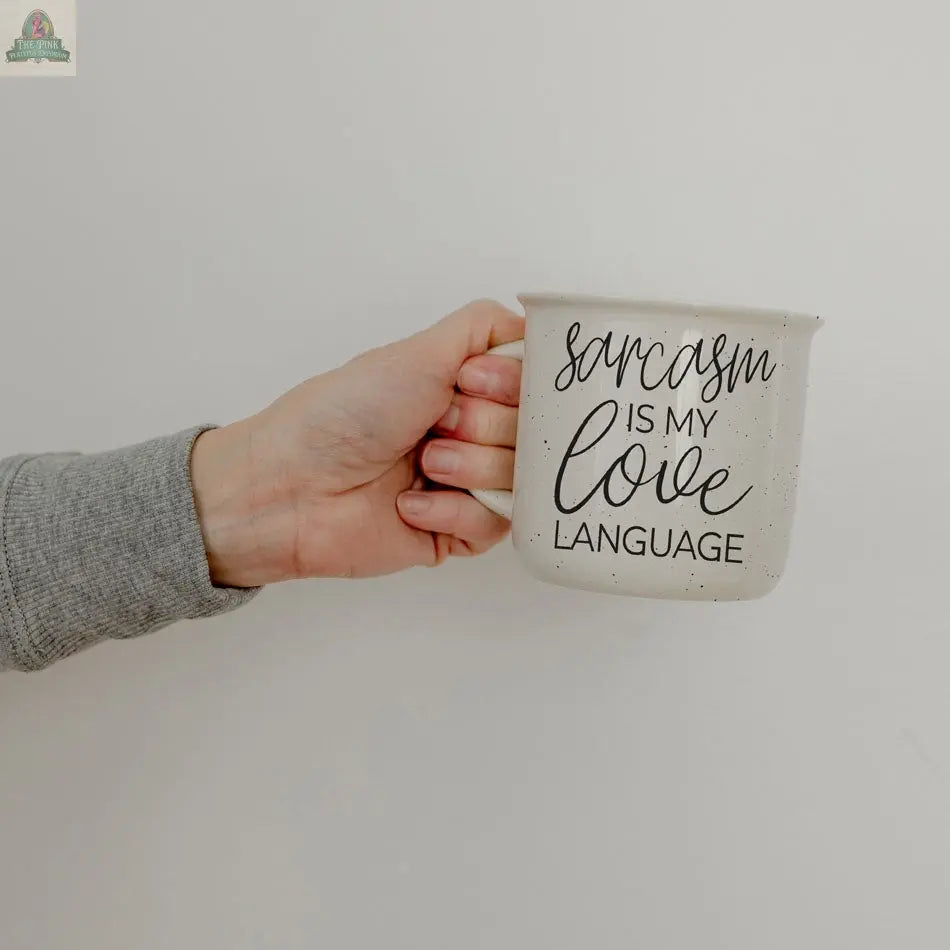 A hand in a gray sleeve holds the Sarcasm Love 14.5oz white ceramic mug, featuring “Sarcasm is my love language” text—a funny coffee mug ideal for anyone who enjoys humor, set against a plain light background.
