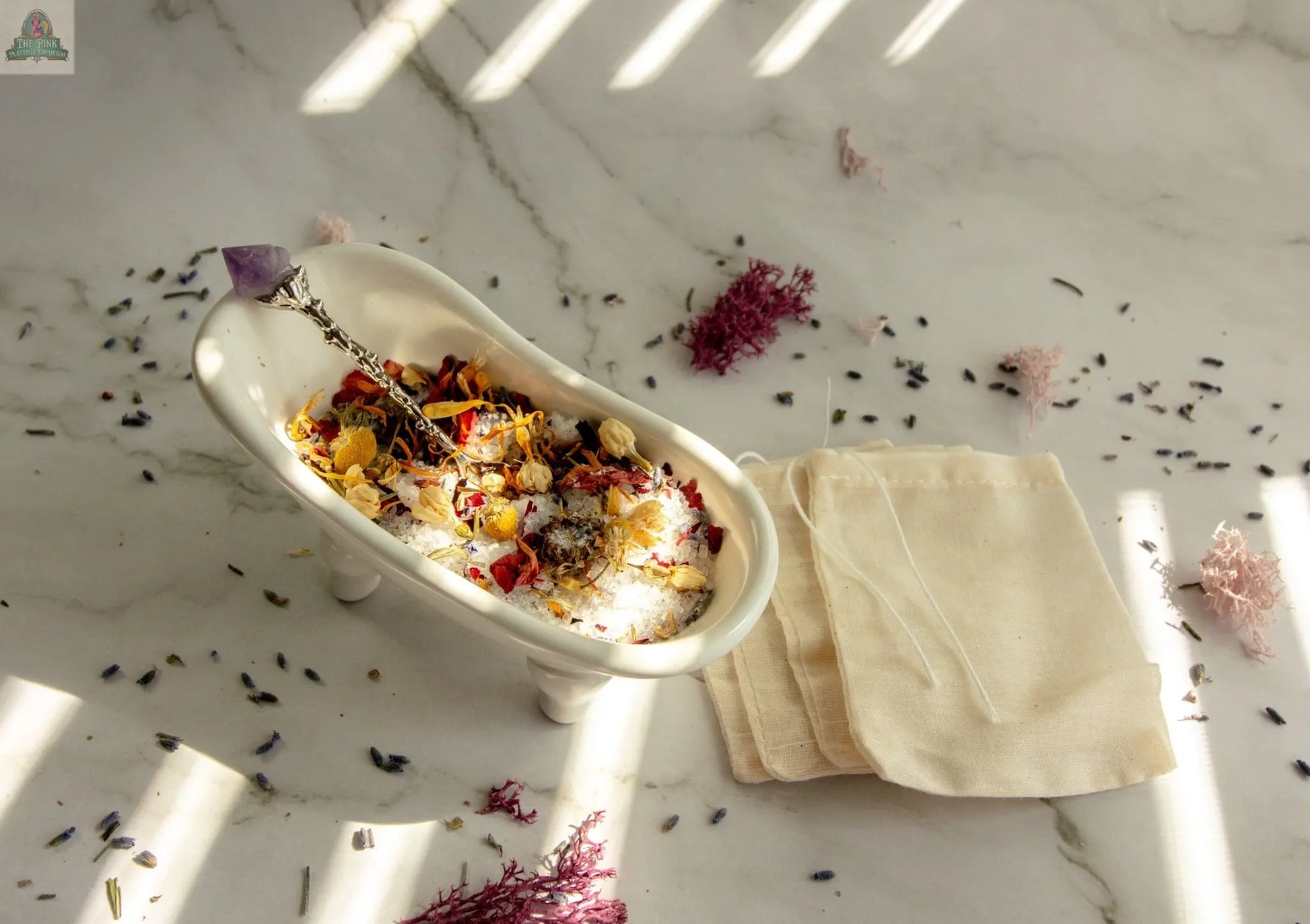 The Self Love set features a small white clawfoot tub dish with dried flowers, bath salts, a decorative spoon, reusable tea bags, scattered herbs, and sunlight, creating a peaceful rose and vanilla essential oil bath tea ritual.