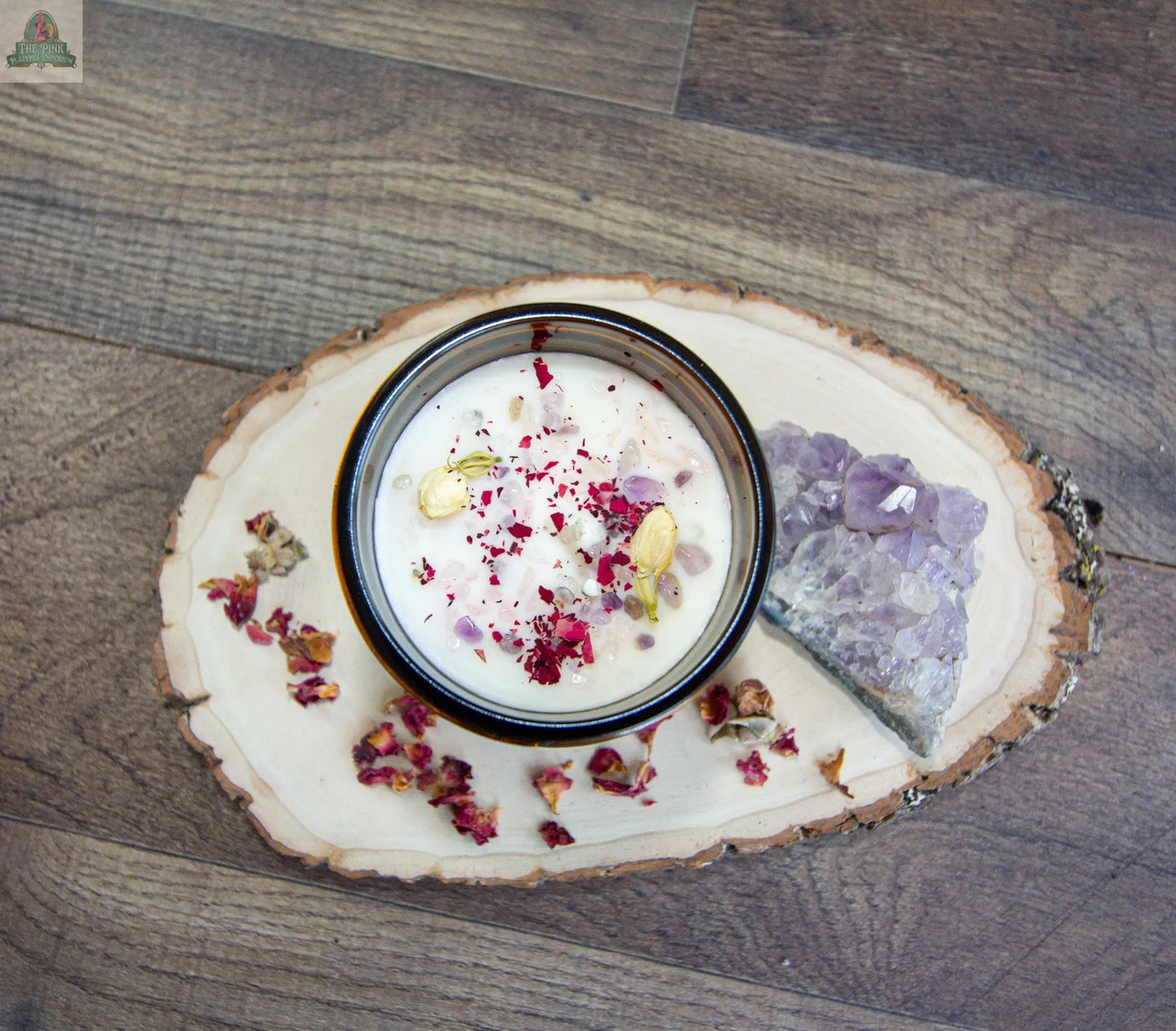A bowl of Self Love yogurt garnished with dried rose petals and cardamom pods sits on a wooden board, with a slice of rose quartz and scattered petals, all beautifully arranged on a wood floor.
