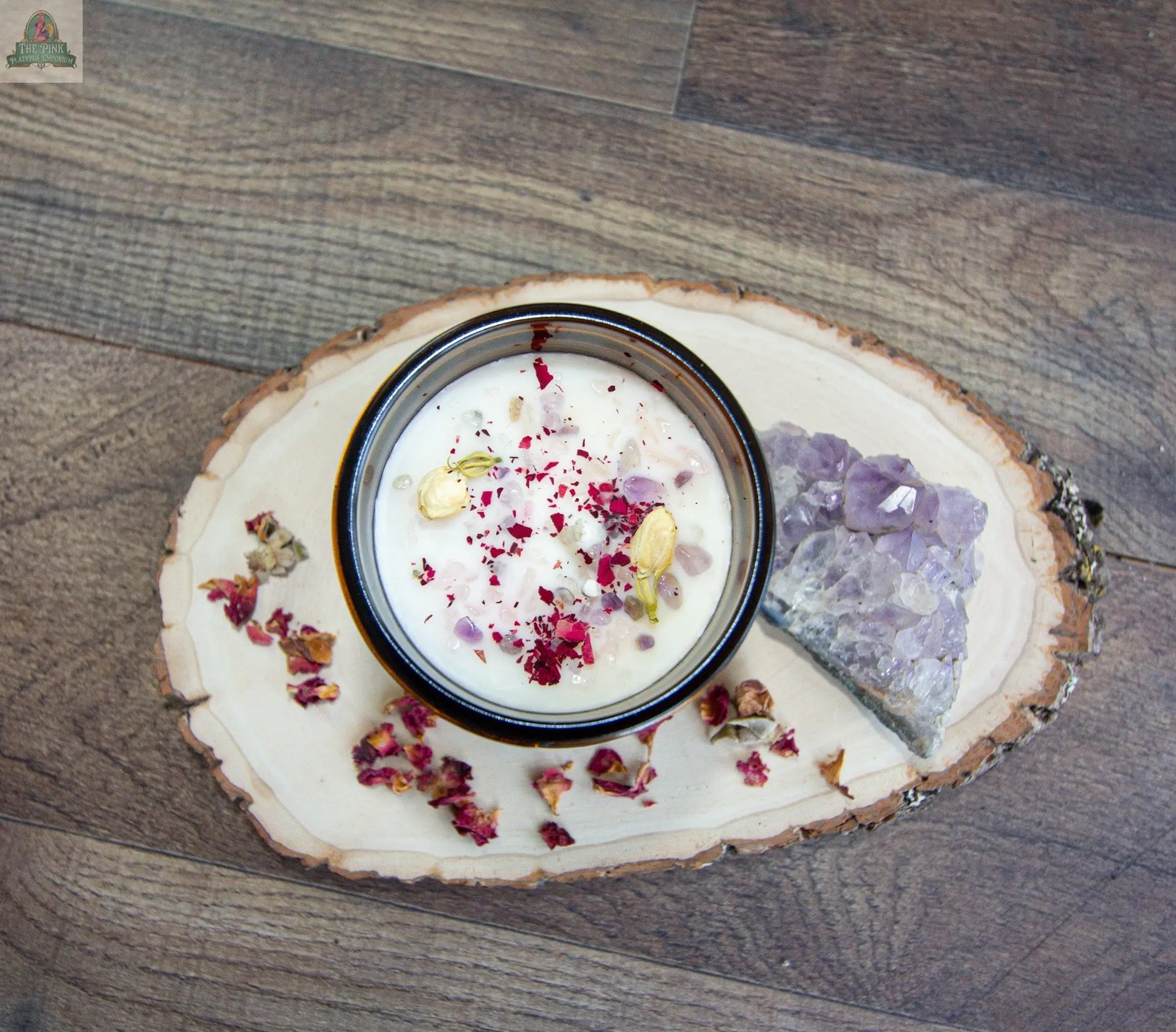 A bowl of Self Love yogurt garnished with dried rose petals and cardamom pods sits on a wooden board, with a slice of rose quartz and scattered petals, all beautifully arranged on a wood floor.