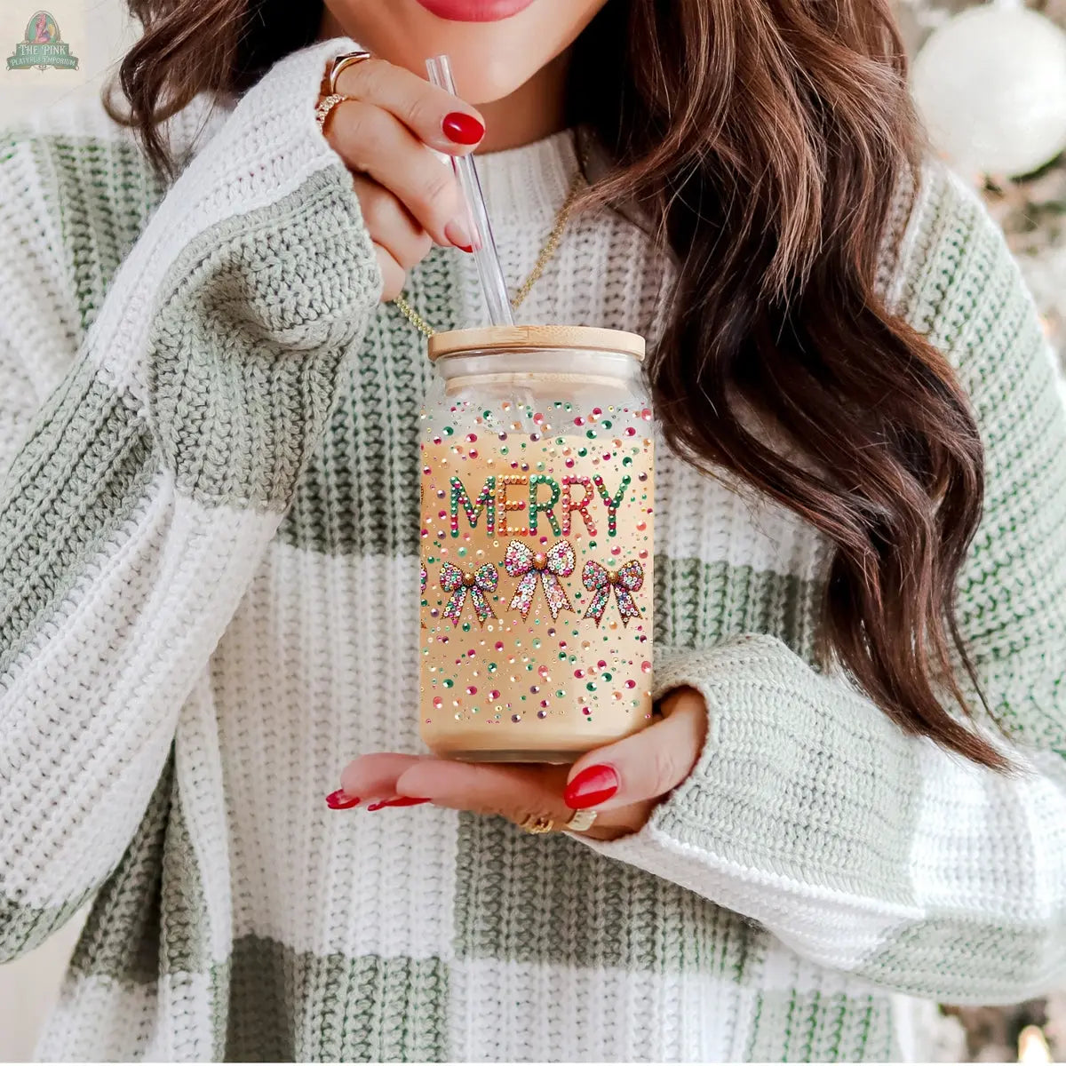 A woman in a green and white striped sweater with long brown hair and red nails sips from a Sequin MERRY holiday tumbler with colorful sprinkles and "MERRY" on it, capturing a festive spirit.