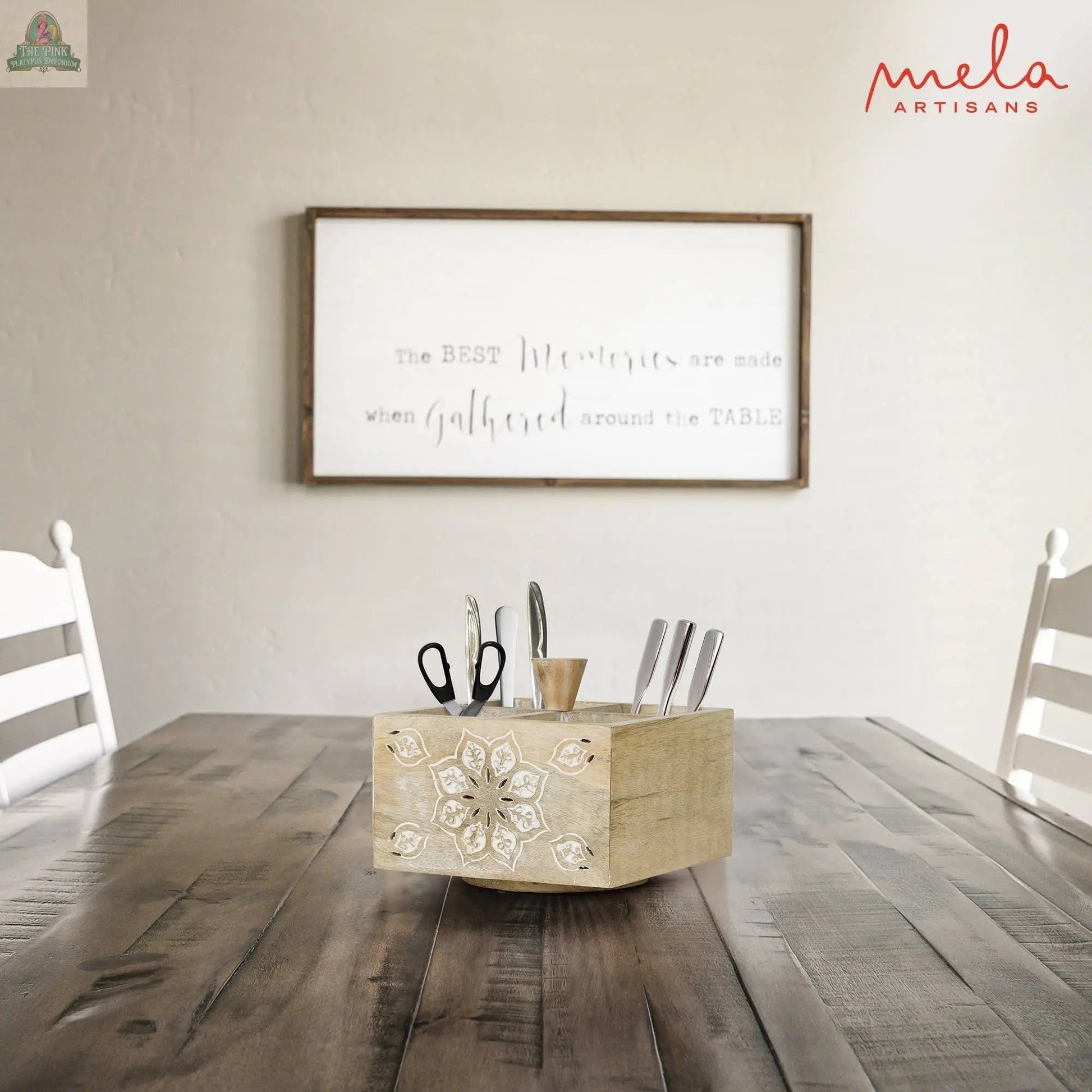A wooden table with white chairs features the Serena Spinner 4 Quad in Whitewash, holding scissors, cutlery, and utensils. In the background, a white wall sign says, “The BEST Memories are made when gathered around the TABLE.”.