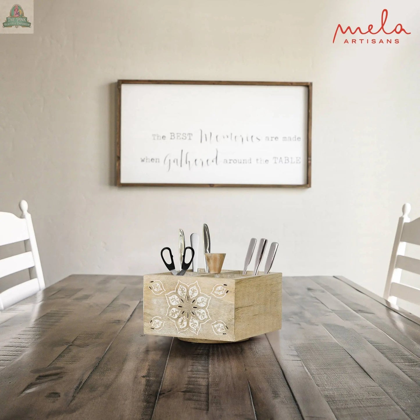 A wooden table with white chairs features the Serena Spinner 4 Quad in Whitewash, holding scissors, cutlery, and utensils. In the background, a white wall sign says, “The BEST Memories are made when gathered around the TABLE.”.