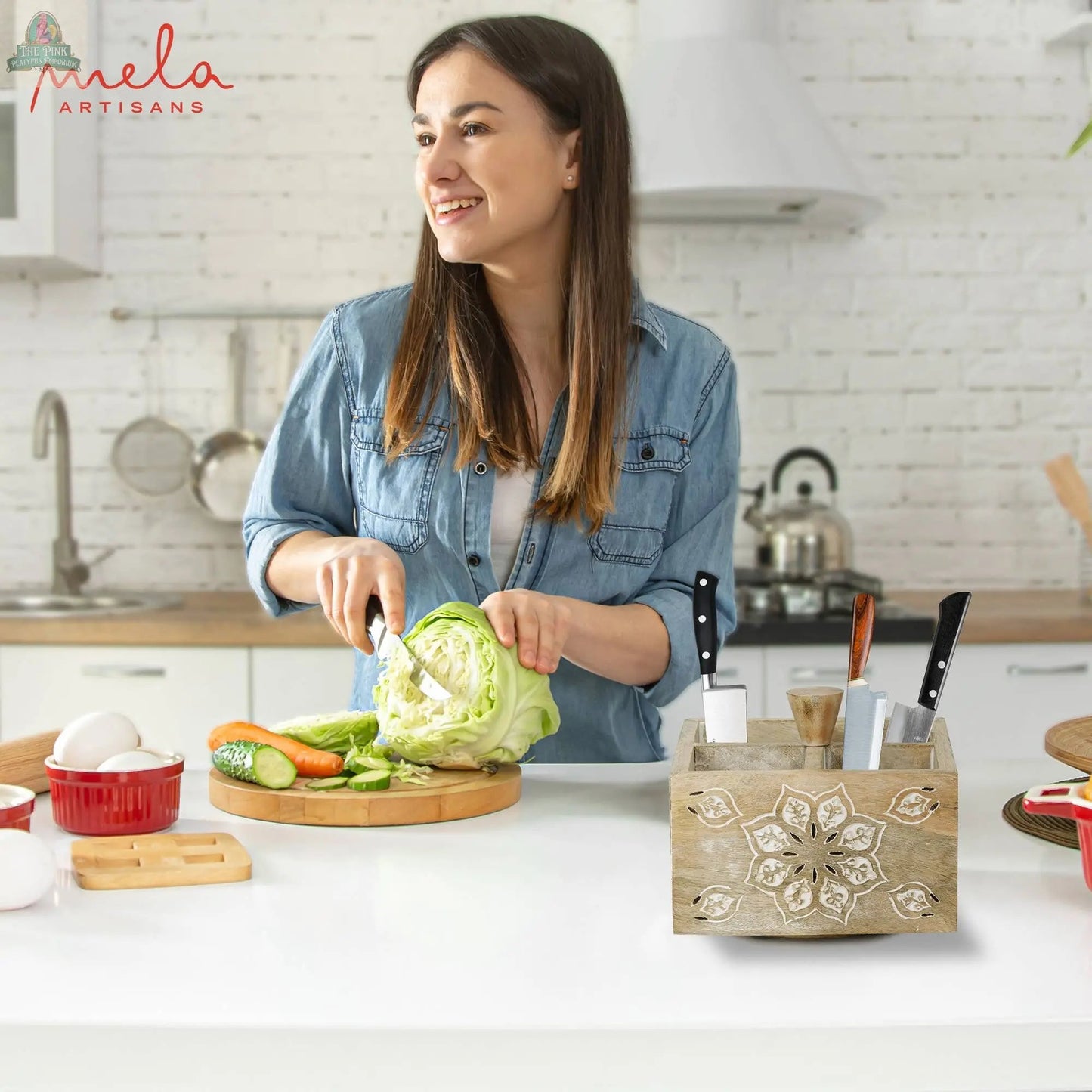A woman in a denim shirt chops cabbage and veggies on a cutting board in a bright, modern kitchen. On the counter is the Serena Spinner 4 Quad in Whitewash. The Mela Artisans logo is visible in the top left corner.
