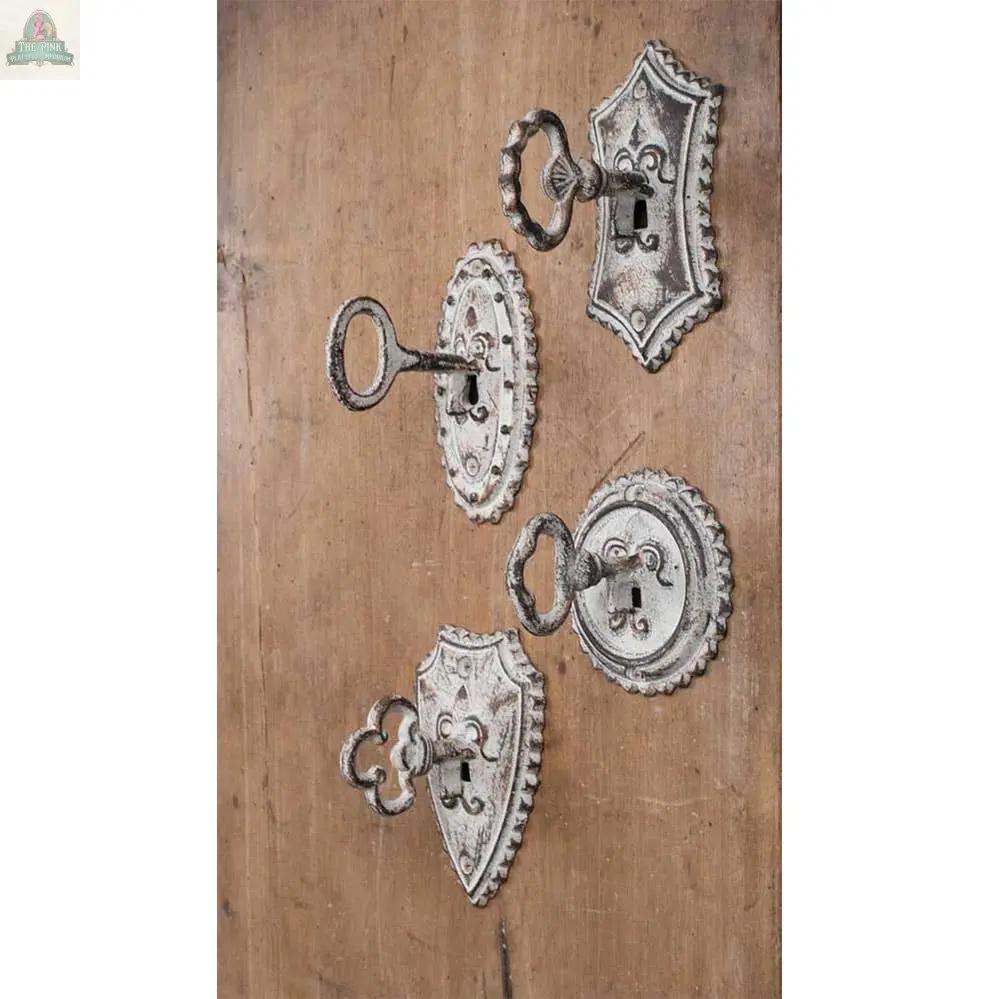 The Set of Four Vintage Key Metal Hooks features unique key-shaped designs with decorative backplates, distressed white finish, and are mounted on wood for an elegant, antique-inspired look.