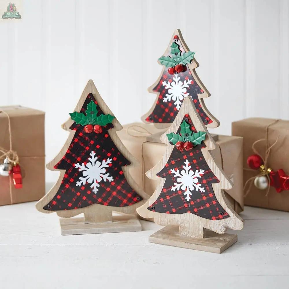 The Set of Three Buffalo Plaid Tabletop Trees features wooden Christmas decorations with red and black plaid, white snowflakes, and holly accents—ideal for festive tabletop trees or Christmas décor. Displayed on a white surface with wrapped gifts in the background.