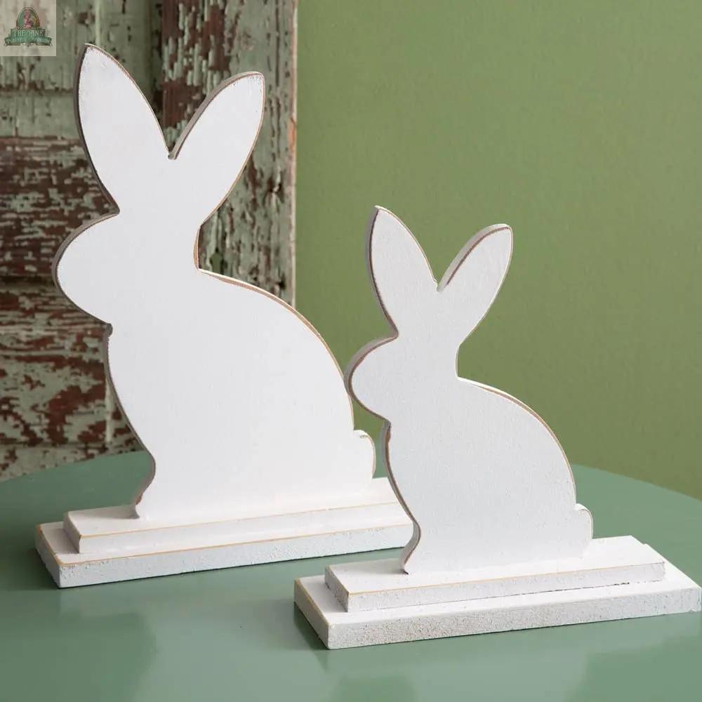 The Set of Two Wooden Bunnies with Metal Cutouts features charming white bunnies on rectangular bases, perfect for rustic decor when displayed against a green surface or wooden background.
