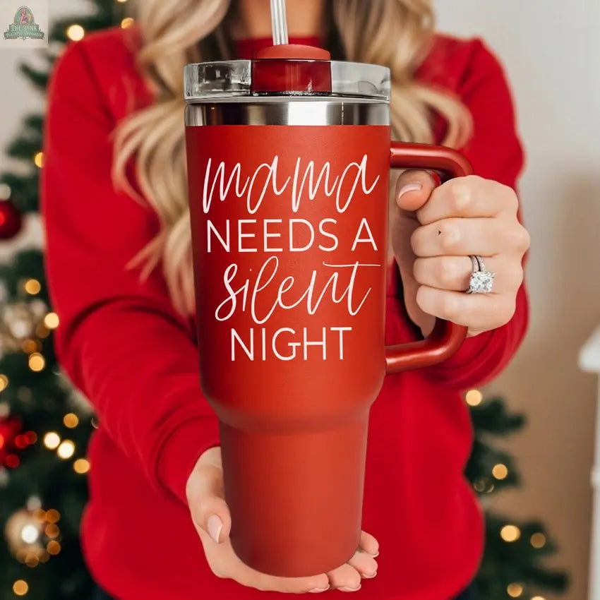 A woman in a red sweater holds the Silent Night 40oz insulated mug with a straw reading "Mama needs a Silent Night," while a decorated Christmas tree glows softly in the background.
