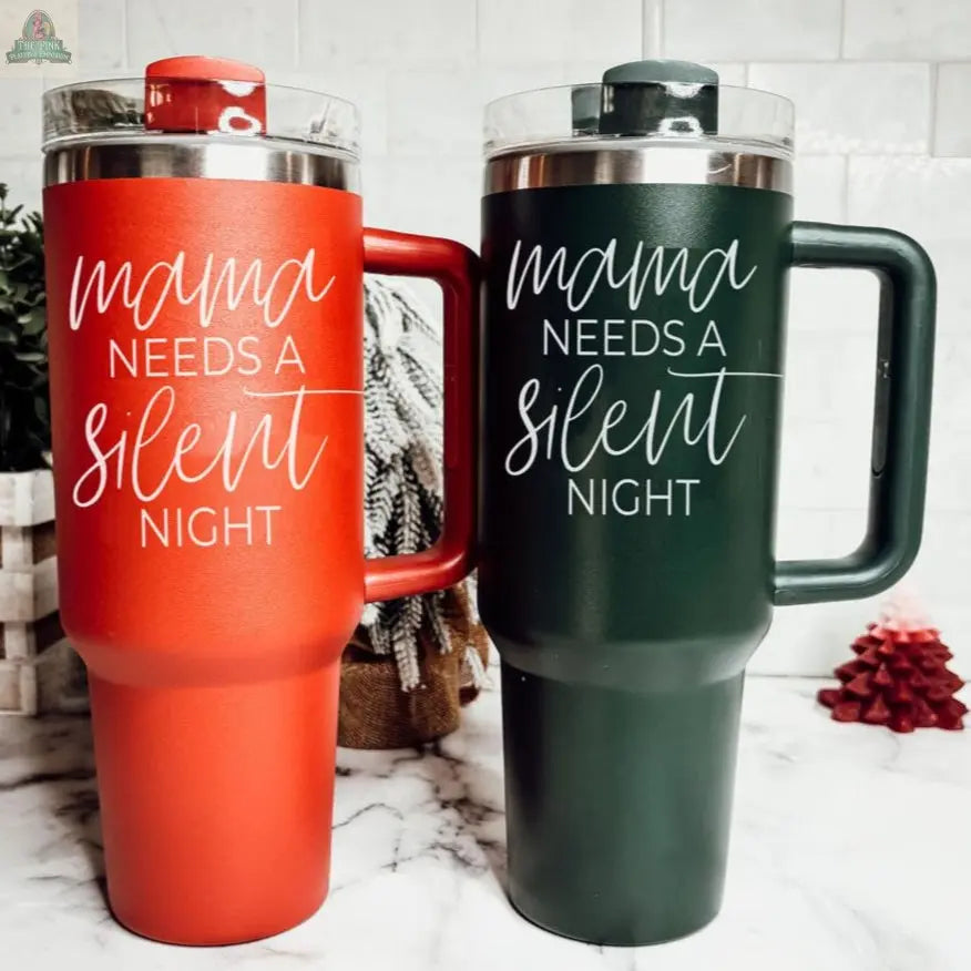 Two 40oz Silent Night tumblers, one red and one green, with clear lids and “Mama needs a silent night” in white script, sit on a marble countertop with holiday decor—perfect as an insulated mug and Christmas gift.
