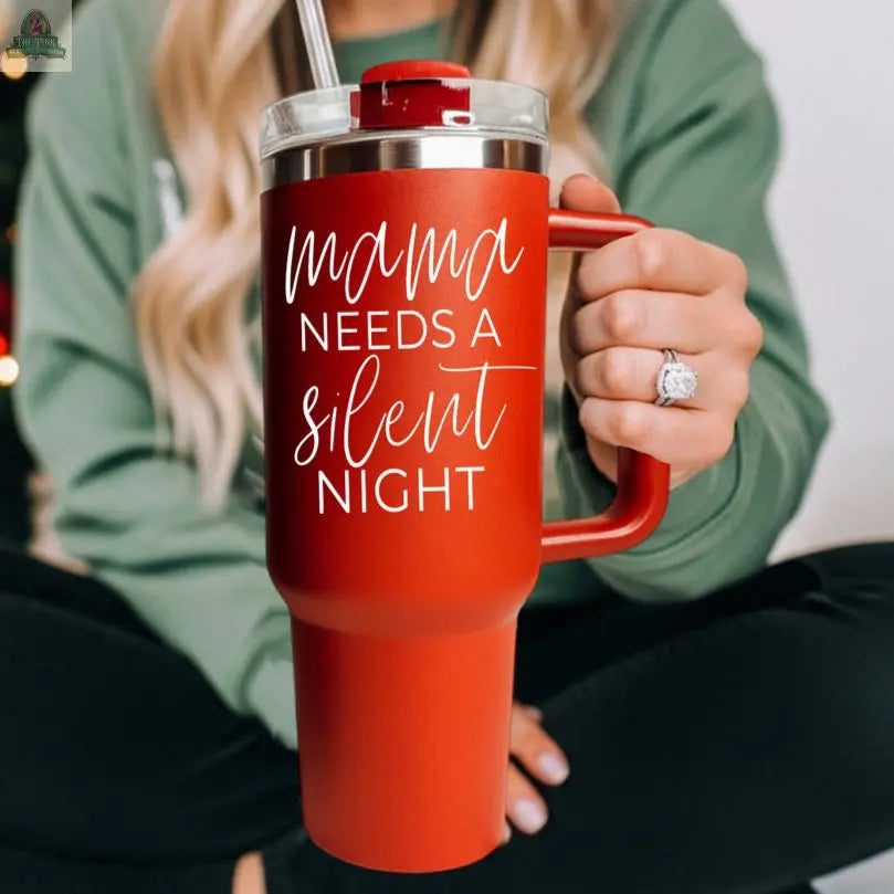 A person with long blonde hair in a green sweater holds the Silent Night 40oz red insulated mug, featuring "Mama needs a silent night" in white script—a cozy Christmas gift idea.