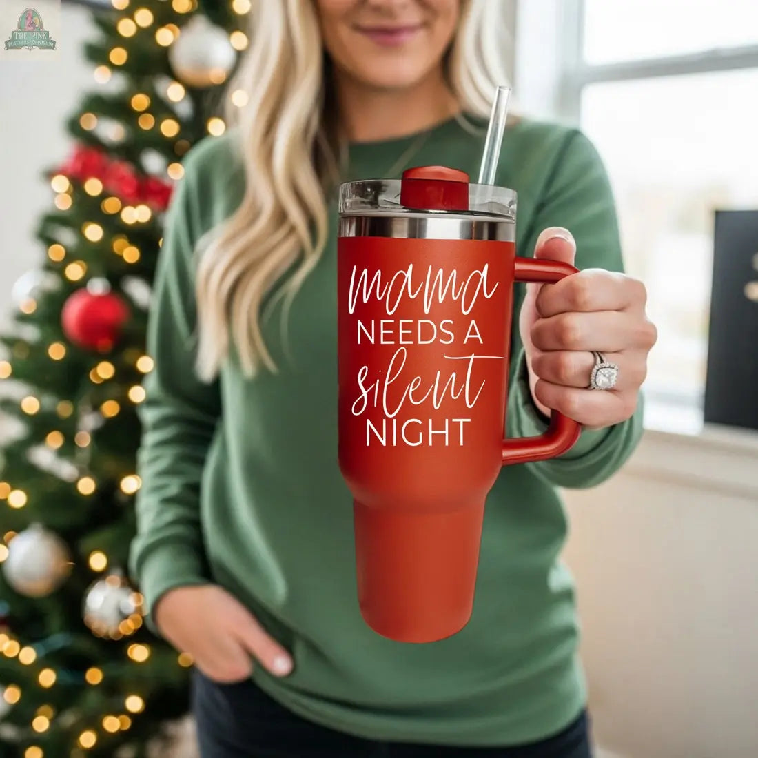 A woman in a green sweater stands by a decorated Christmas tree, holding the Silent Night 40oz mug with "Mama needs a silent night" in white script—an ideal Christmas gift.